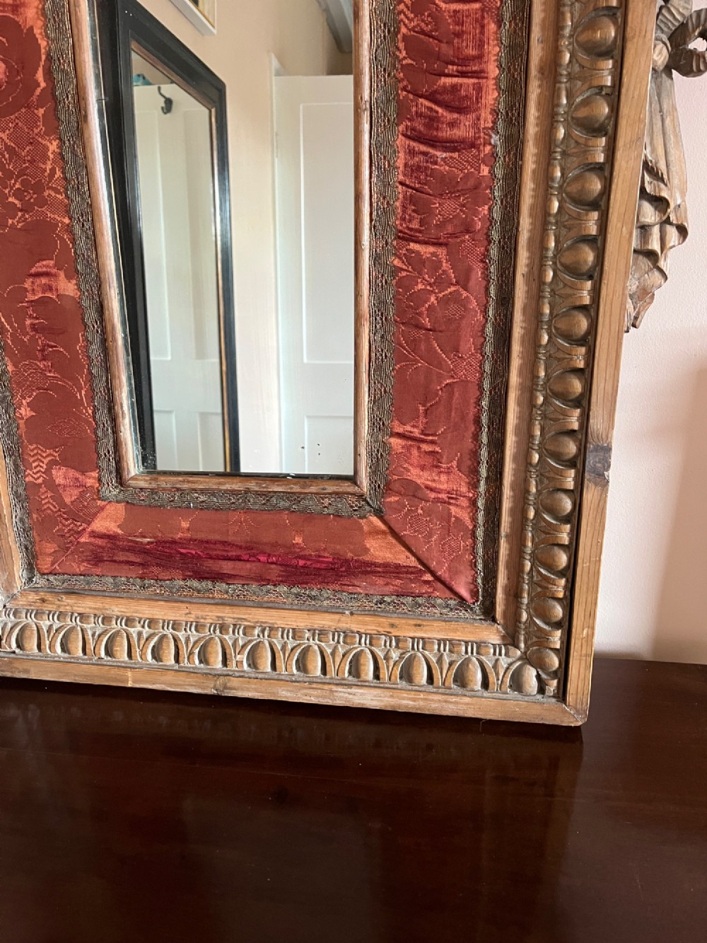 An 18th-century carved pine wall mirror featuring egg-and-dart outer borders, side ear brackets, and a red damask fabric panel surrounding the central rectangular glass plate. View III