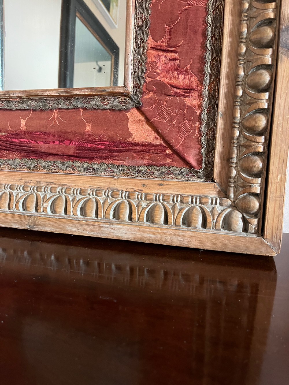 An 18th-century carved pine wall mirror featuring egg-and-dart outer borders, side ear brackets, and a red damask fabric panel surrounding the central rectangular glass plate. View IV