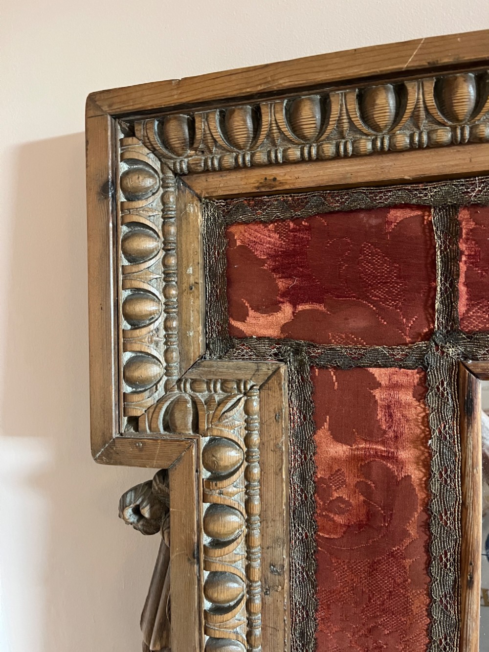 An 18th-century carved pine wall mirror featuring egg-and-dart outer borders, side ear brackets, and a red damask fabric panel surrounding the central rectangular glass plate. View V