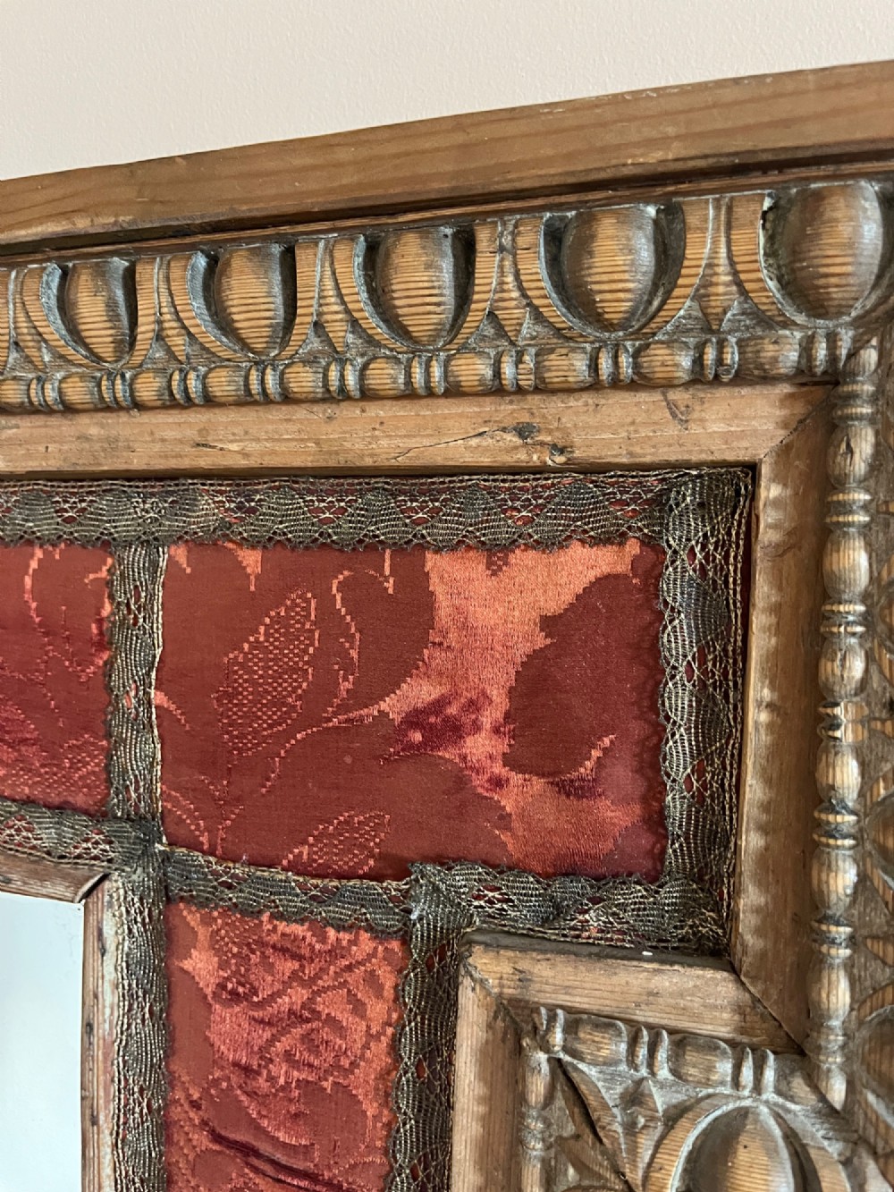 An 18th-century carved pine wall mirror featuring egg-and-dart outer borders, side ear brackets, and a red damask fabric panel surrounding the central rectangular glass plate. View VII