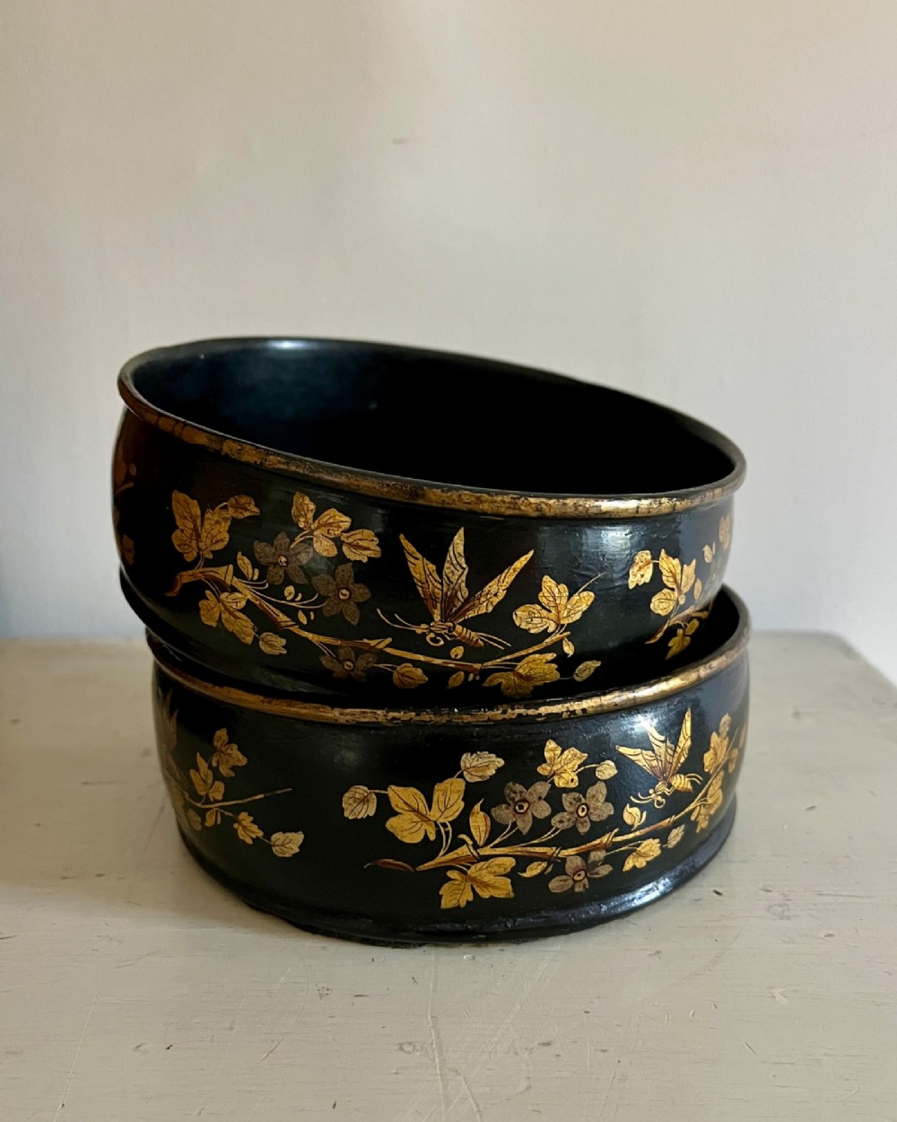A pair of circular black lacquered papier-mache wine coasters decorated with hand-painted gold botanical and dragonfly motifs. View II