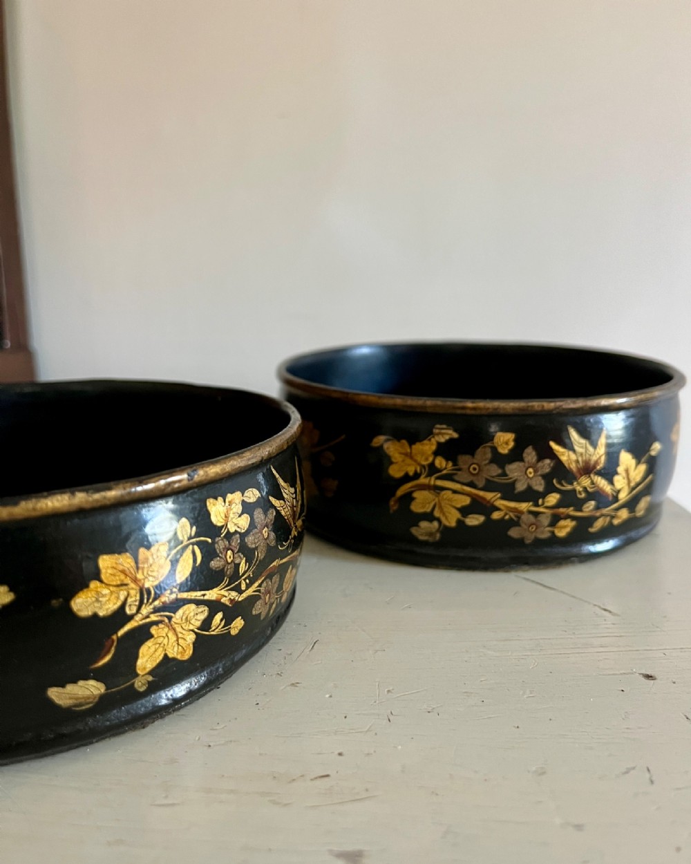 A pair of circular black lacquered papier-mache wine coasters decorated with hand-painted gold botanical and dragonfly motifs. View III