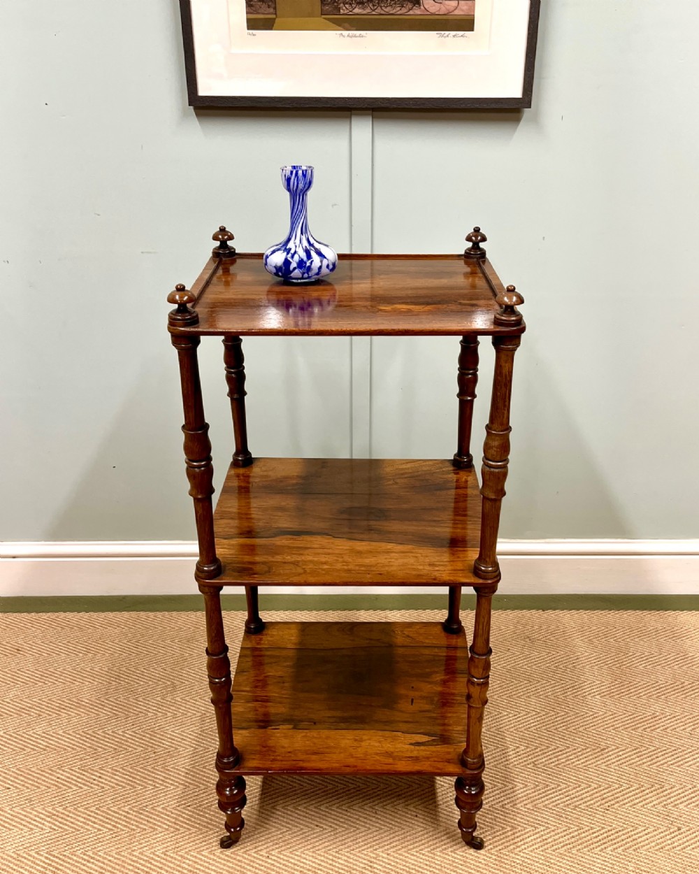 A 19th-century rosewood three-tier etagere featuring turned spindle corner posts, top finials, and brass castors on the feet. View II
