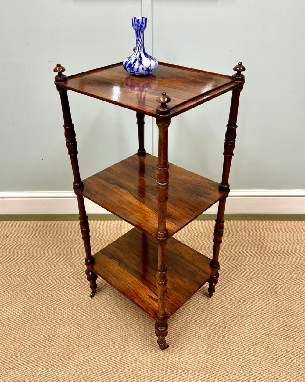 A 19th-century rosewood three-tier etagere featuring turned spindle corner posts, top finials, and brass castors on the feet. View IV