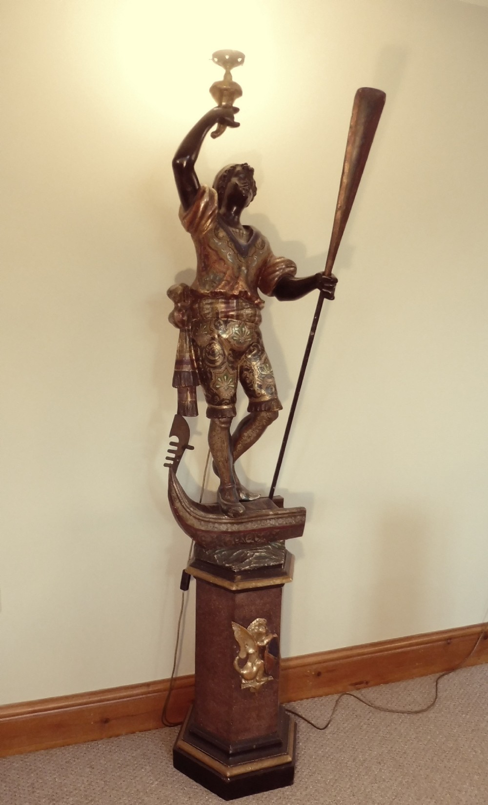 A carved Venetian figural standard lamp depicting a standing gondolier holding an oar atop a pedestal.