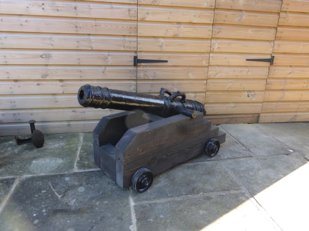 A 19th-century French cast iron cannon barrel with raised mouldings and dolphin handles, mounted on a dark timber wheeled carriage.