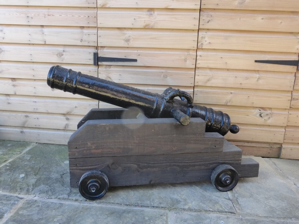 A 19th-century French cast iron cannon barrel with raised mouldings and dolphin handles, mounted on a dark timber wheeled carriage. View V