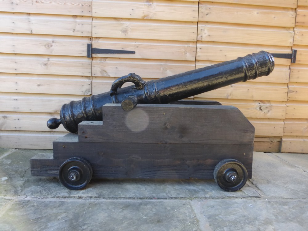 A 19th-century French cast iron cannon barrel with raised mouldings and dolphin handles, mounted on a dark timber wheeled carriage. View VI