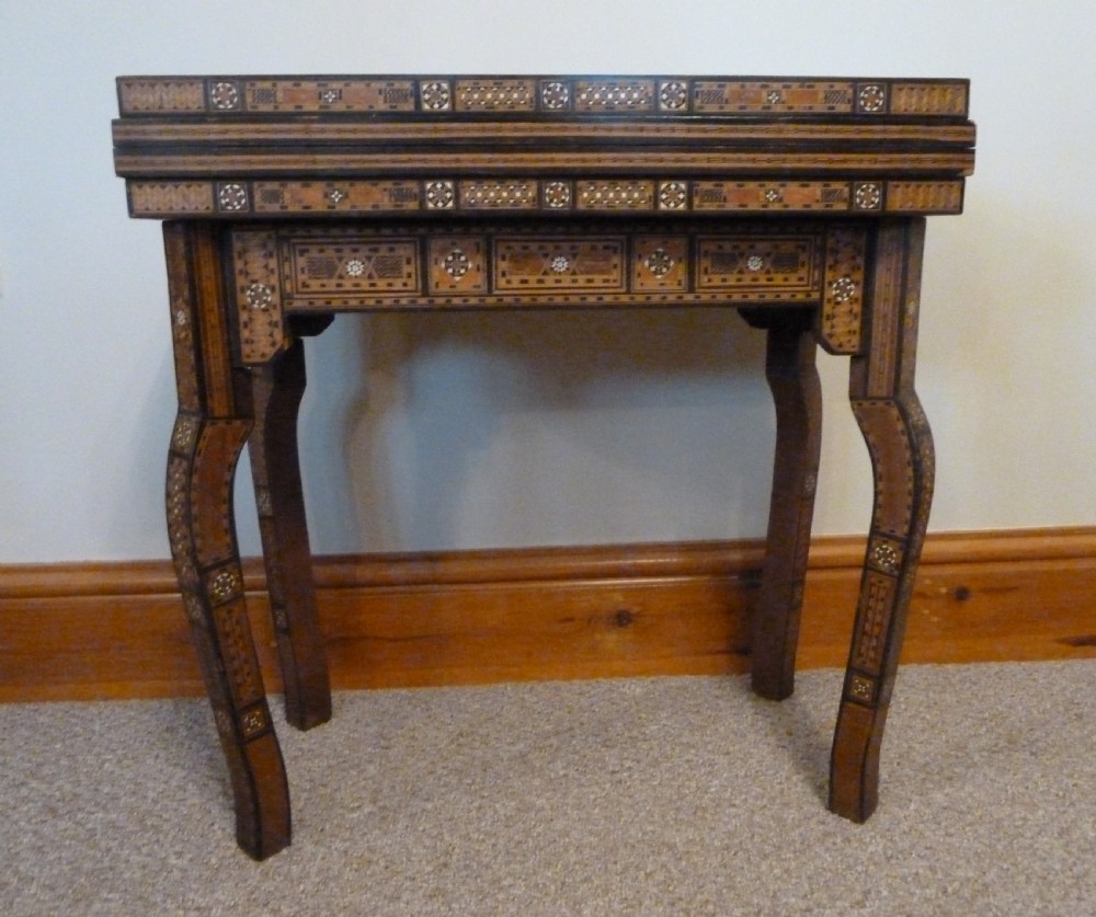 A Syrian Damascus card table featuring geometric wood and bone inlay work supported by curved cabriole legs.