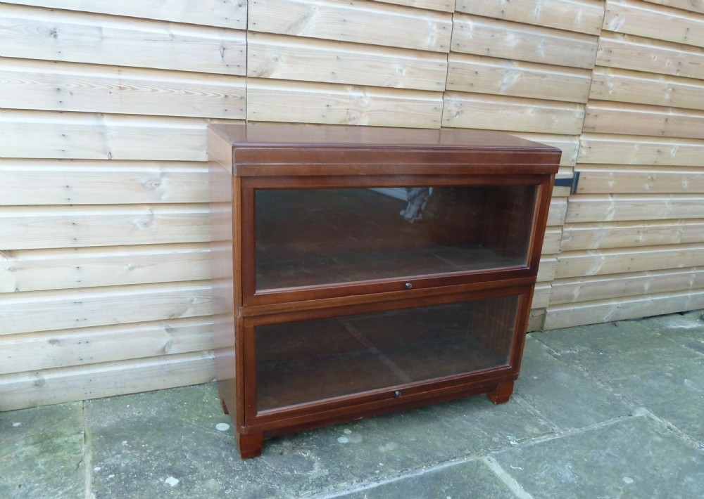 An Art Deco two-tier modular wood sectional bookcase featuring glass up-and-over doors and square block feet.