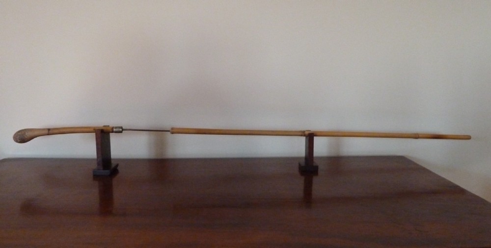 An antique bamboo swordstick shown partially unsheathed to reveal a concealed steel blade, featuring a natural bamboo handle and metal collar band.