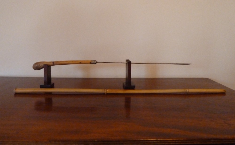 An antique bamboo swordstick shown partially unsheathed to reveal a concealed steel blade, featuring a natural bamboo handle and metal collar band. View VII