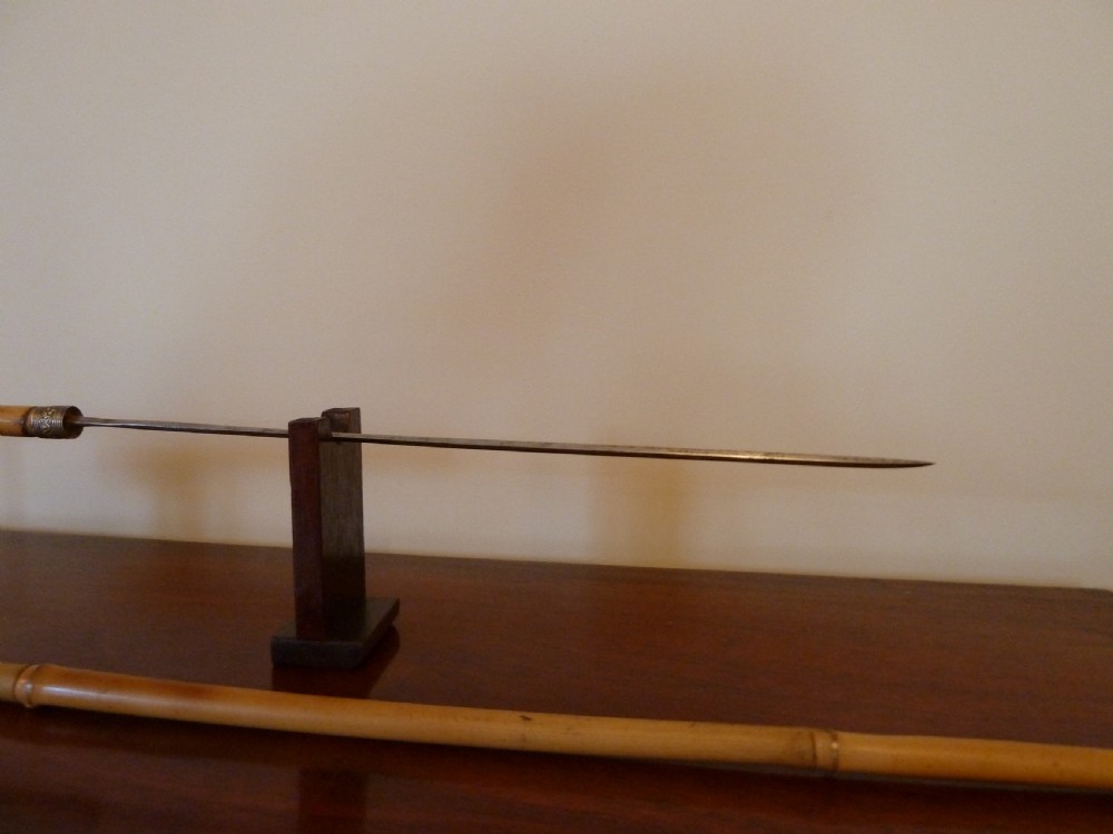 An antique bamboo swordstick shown partially unsheathed to reveal a concealed steel blade, featuring a natural bamboo handle and metal collar band. View IX