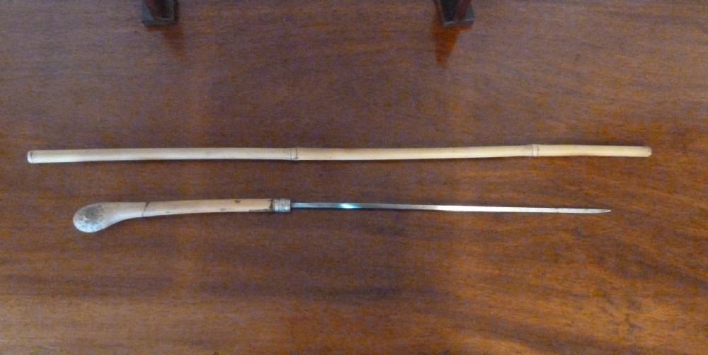 An antique bamboo swordstick shown partially unsheathed to reveal a concealed steel blade, featuring a natural bamboo handle and metal collar band. View X