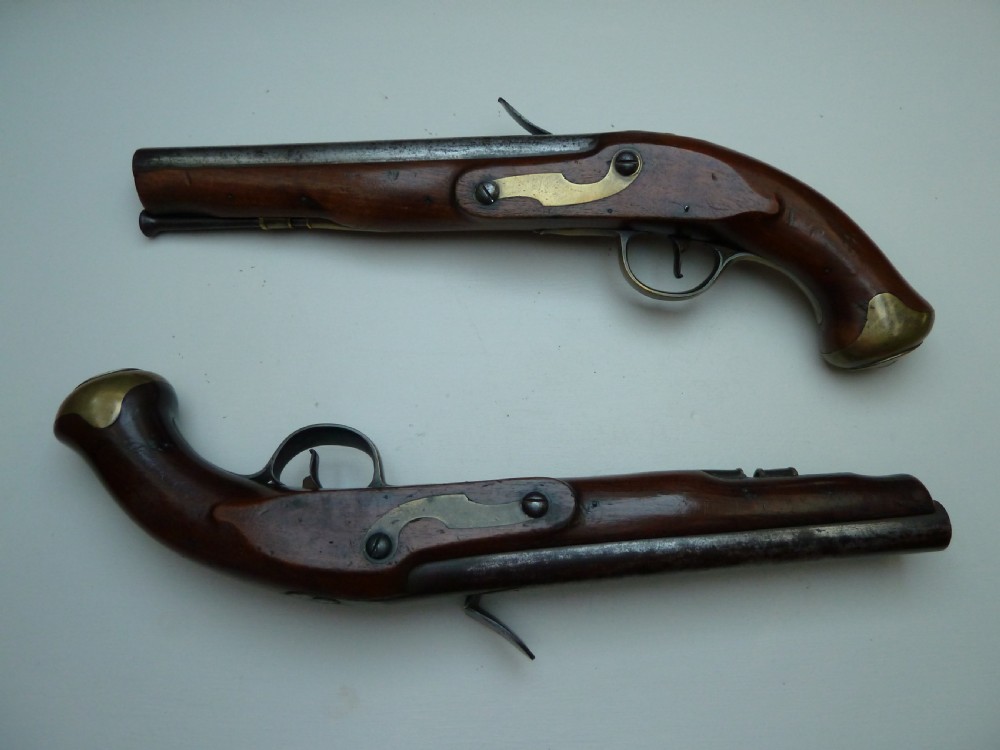A pair of early 19th-century flintlock duelling pistols featuring contoured wooden stocks, brass sideplates, and steel barrels.