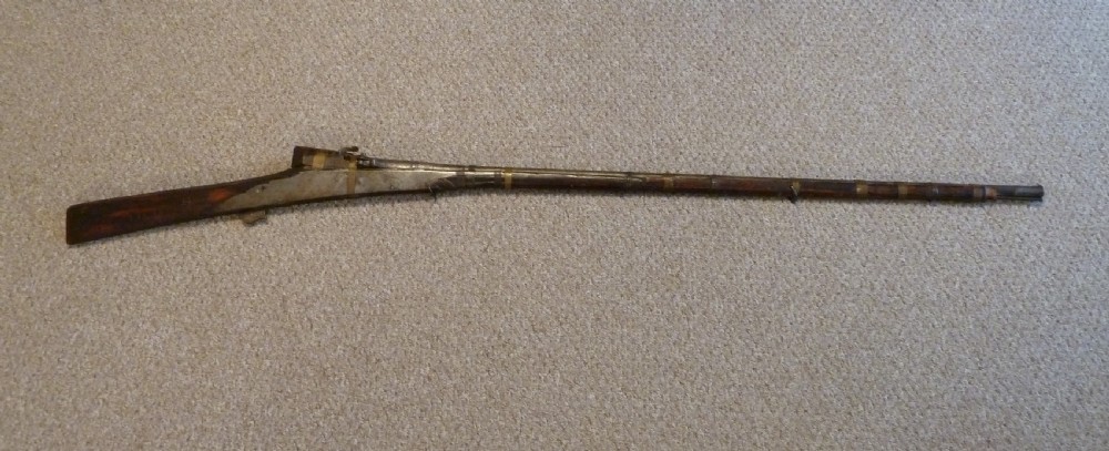 An antique Indian matchlock Torador musket featuring a long steel barrel bound with brass straps to a dark wood stock.