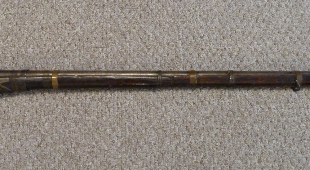 An antique Indian matchlock Torador musket featuring a long steel barrel bound with brass straps to a dark wood stock. View III