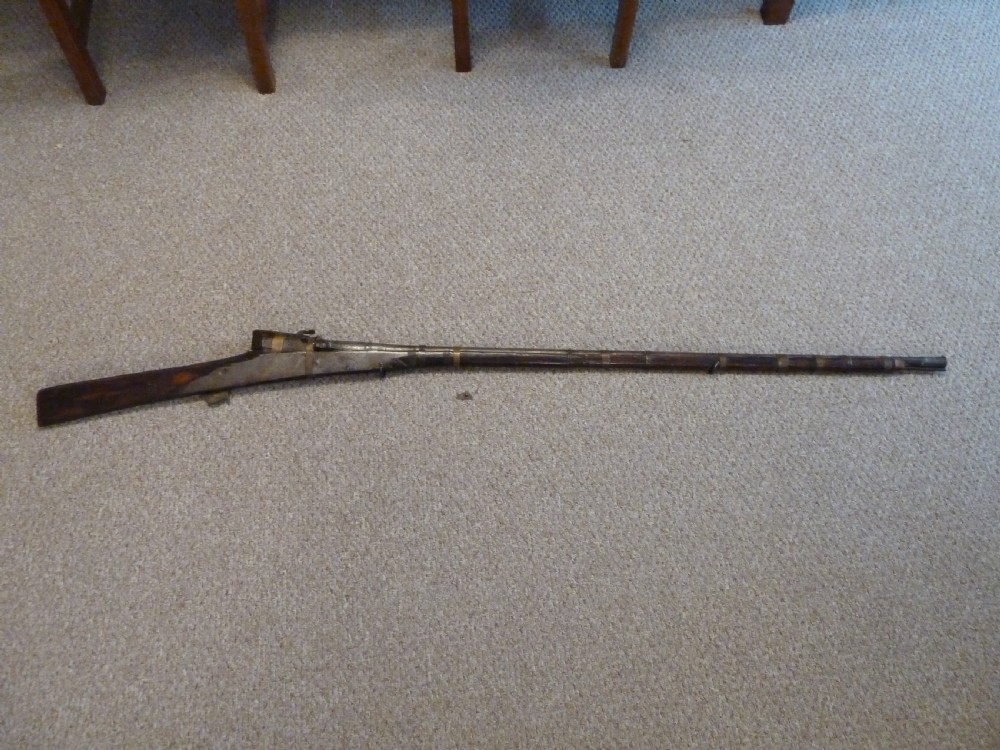 An antique Indian matchlock Torador musket featuring a long steel barrel bound with brass straps to a dark wood stock. View X