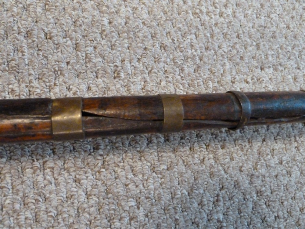 An antique Indian matchlock Torador musket featuring a long steel barrel bound with brass straps to a dark wood stock. View XII