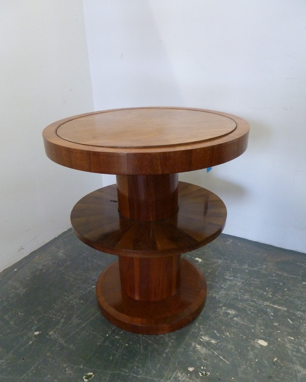 A circular Art Deco walnut metamorphic card table featuring a quarter-veneered top, central cylindrical column, and tiered circular shelf. View V