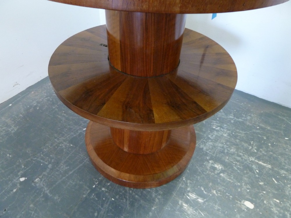A circular Art Deco walnut metamorphic card table featuring a quarter-veneered top, central cylindrical column, and tiered circular shelf. View VI