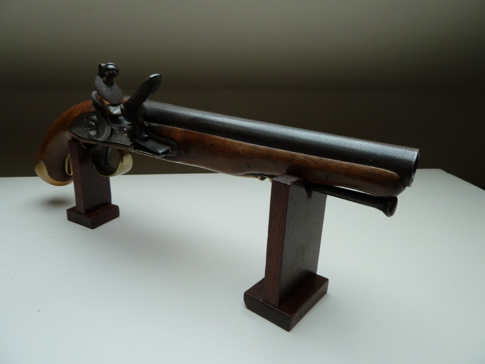 An 18th-century flintlock pistol featuring a carved dark walnut stock, a steel barrel and flint mechanism, and a brass butt cap. View V