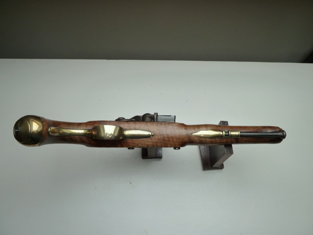 An 18th-century flintlock pistol featuring a carved dark walnut stock, a steel barrel and flint mechanism, and a brass butt cap. View X