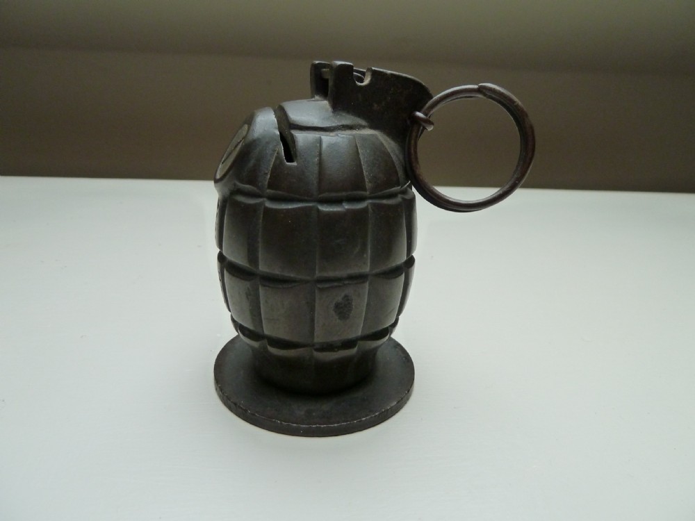 A dark cast iron money box shaped like a First World War hand grenade with a top pull ring and coin slot.