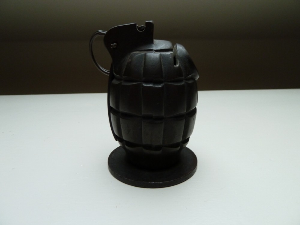 A dark cast iron money box shaped like a First World War hand grenade with a top pull ring and coin slot. View III