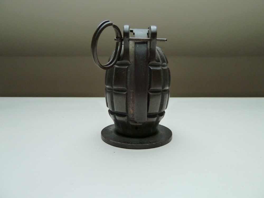 A dark cast iron money box shaped like a First World War hand grenade with a top pull ring and coin slot. View IV