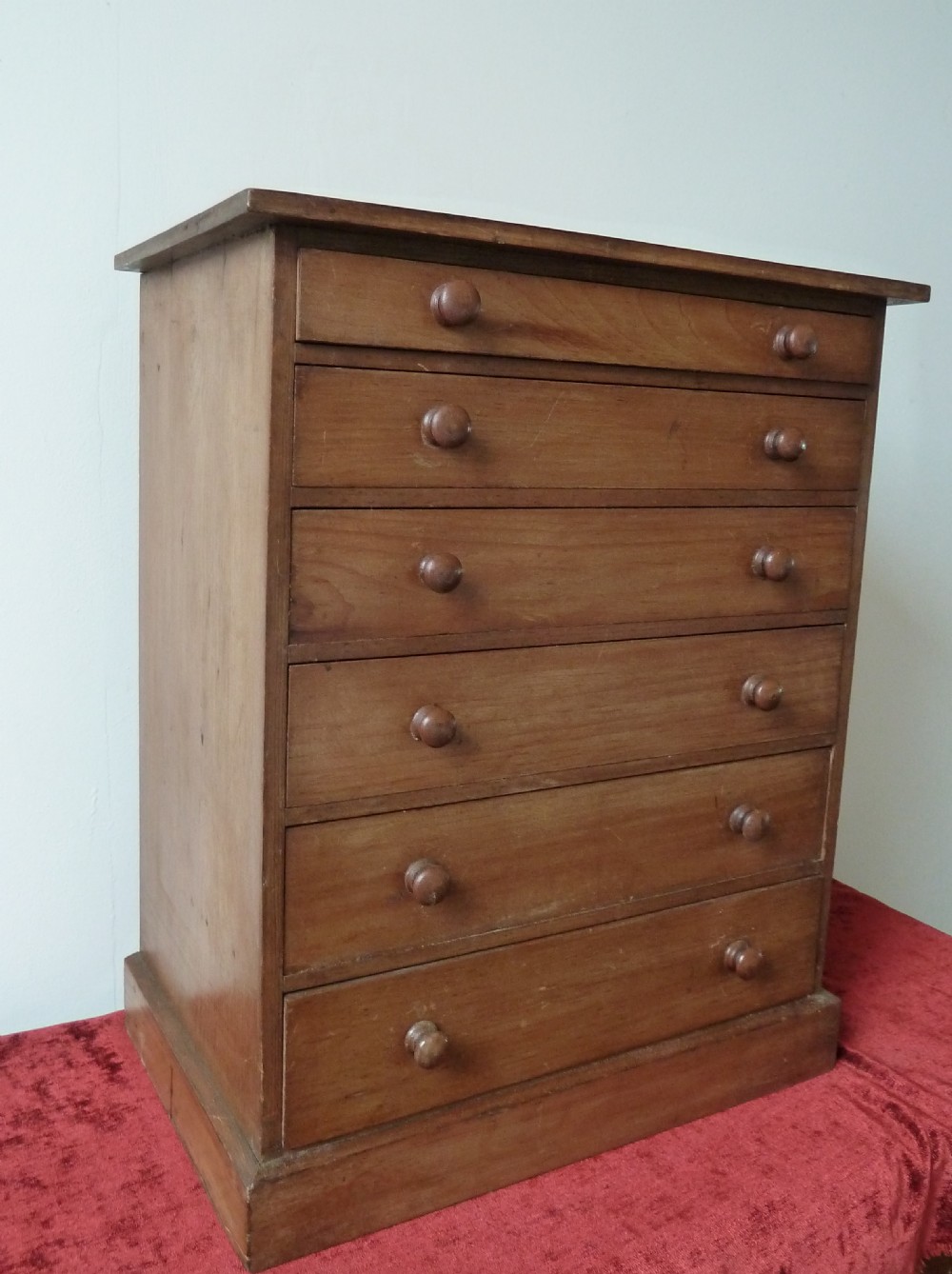 A Victorian pine chest featuring six shallow drawers with turned wooden knobs and a solid plinth base. View VI