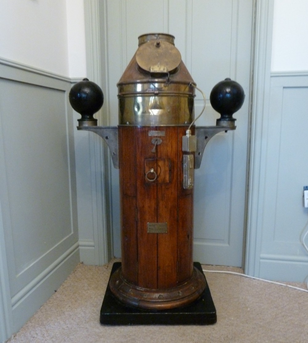 A 19th-century floor-standing ships binnacle featuring a polished brass hood with a glass viewing window, a wooden cylindrical pedestal, and two black iron spheres mounted on side brackets. View II