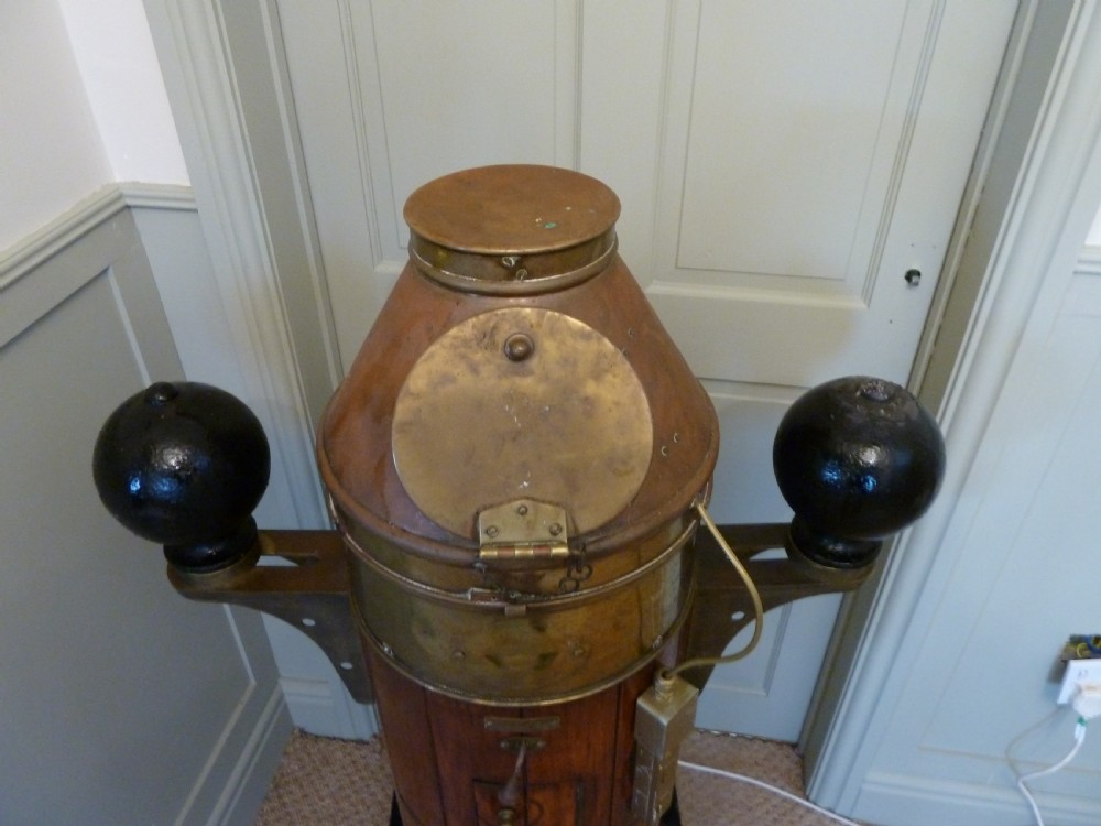 A 19th-century floor-standing ships binnacle featuring a polished brass hood with a glass viewing window, a wooden cylindrical pedestal, and two black iron spheres mounted on side brackets. View V