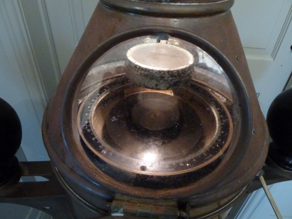 A 19th-century floor-standing ships binnacle featuring a polished brass hood with a glass viewing window, a wooden cylindrical pedestal, and two black iron spheres mounted on side brackets. View VI