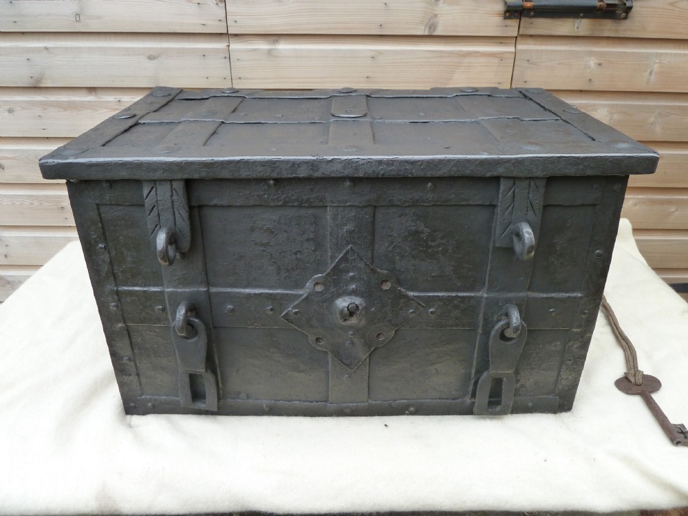A heavy 17th-century black wrought iron Armada chest with external iron strapwork, side drop handles, and a key sticking out from the top lid. View II