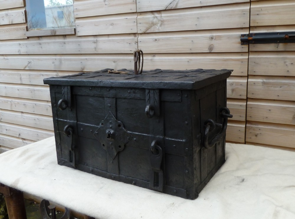 A heavy 17th-century black wrought iron Armada chest with external iron strapwork, side drop handles, and a key sticking out from the top lid. View XVII
