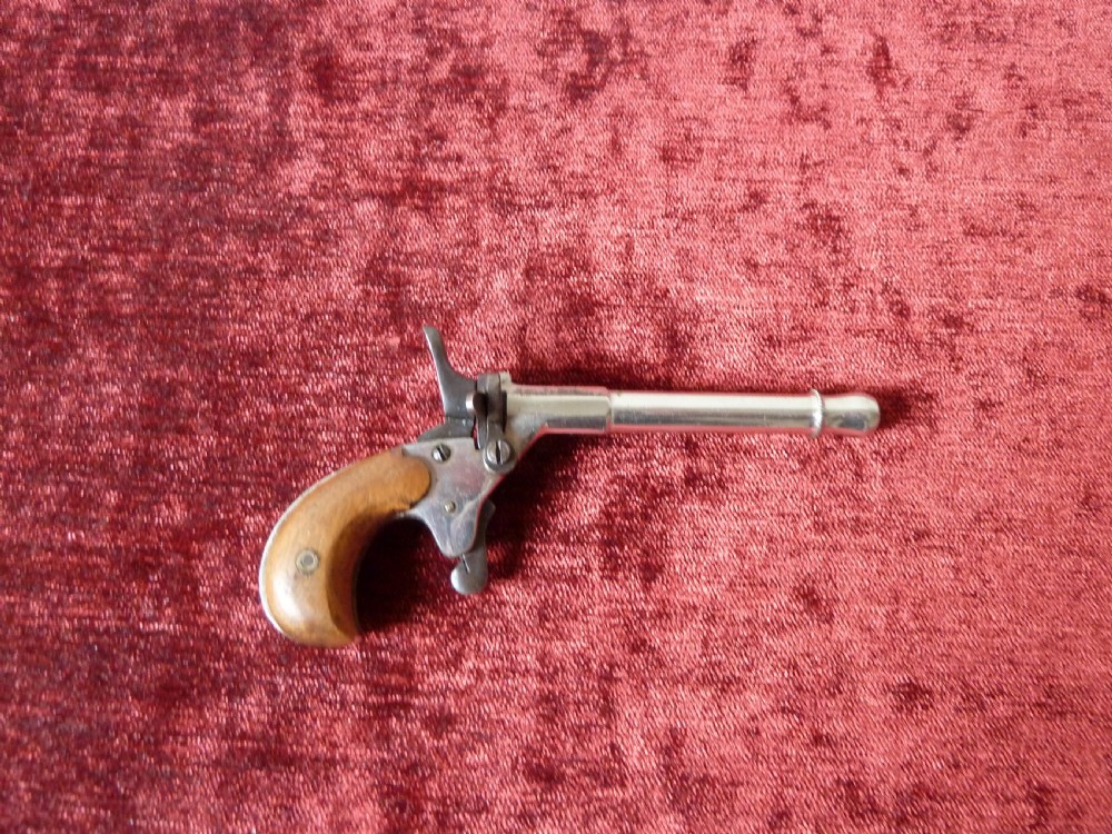 A small 19th-century postmans dog scarer pistol featuring a turned metal barrel, exposed hammer mechanism, and contoured wooden handle.