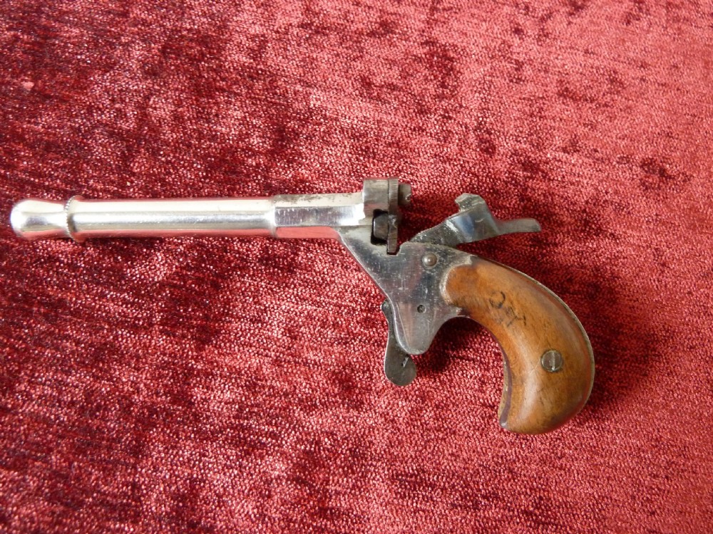 A small 19th-century postmans dog scarer pistol featuring a turned metal barrel, exposed hammer mechanism, and contoured wooden handle. View III