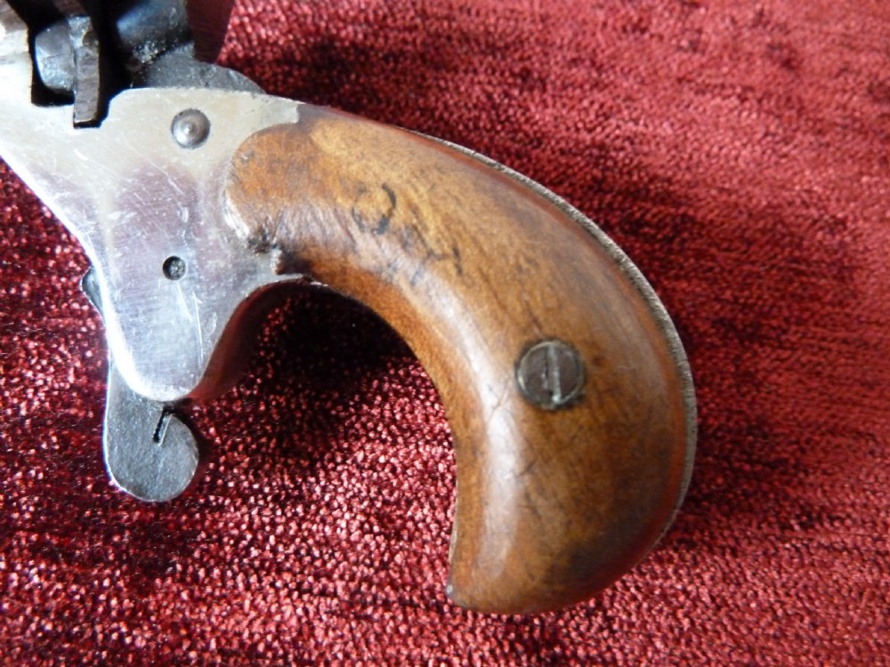 A small 19th-century postmans dog scarer pistol featuring a turned metal barrel, exposed hammer mechanism, and contoured wooden handle. View V