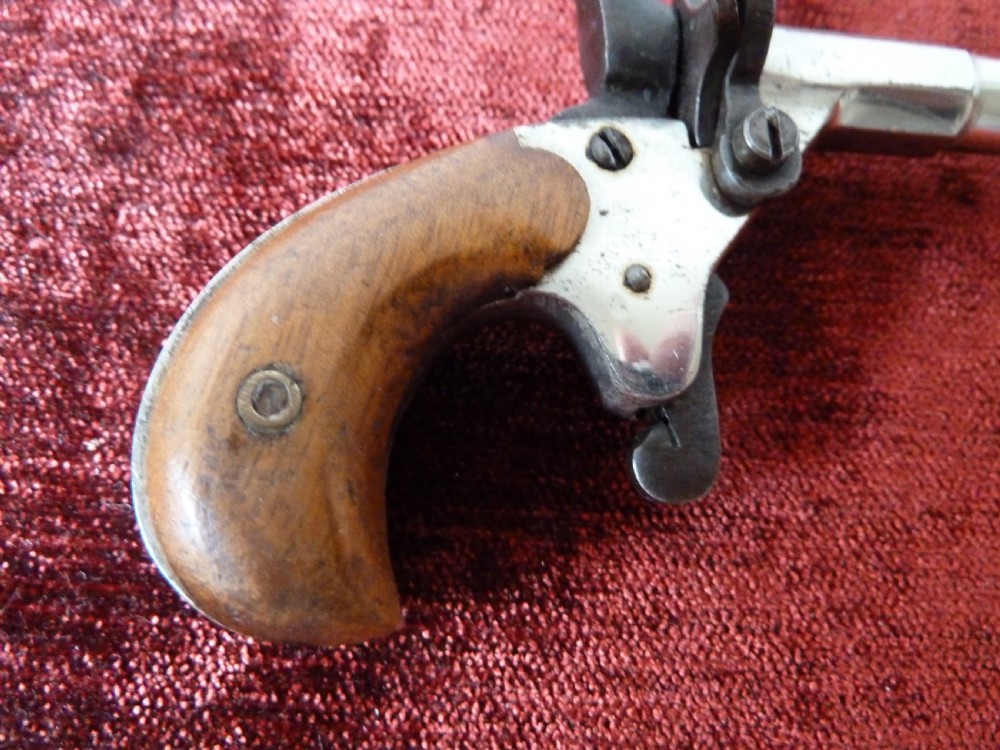 A small 19th-century postmans dog scarer pistol featuring a turned metal barrel, exposed hammer mechanism, and contoured wooden handle. View VI
