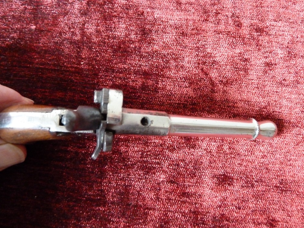 A small 19th-century postmans dog scarer pistol featuring a turned metal barrel, exposed hammer mechanism, and contoured wooden handle. View VII
