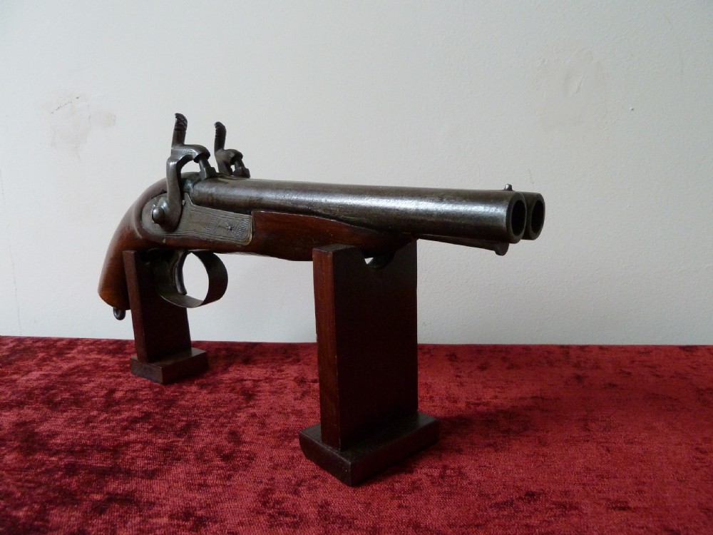 A 19th-century double-barrel percussion pistol featuring side-by-side steel barrels, dual hammers, engraved lockplates, and a smooth walnut stock.