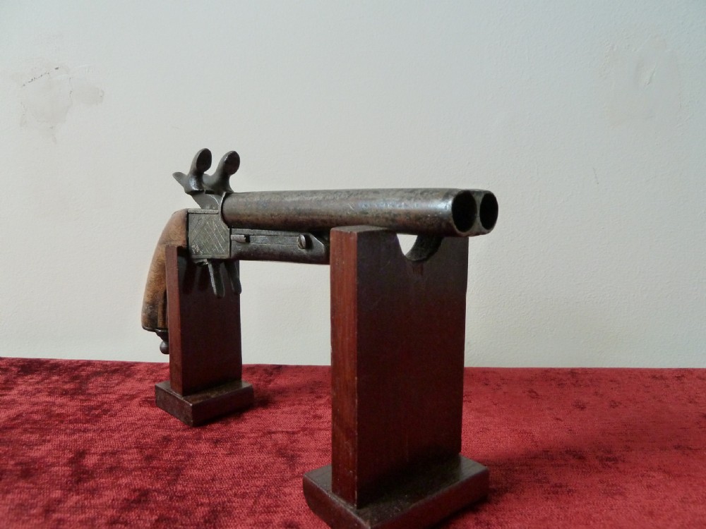 A nineteenth-century double-barrelled rimfire pistol with patinated steel barrels and a contoured wooden grip resting on display stands.