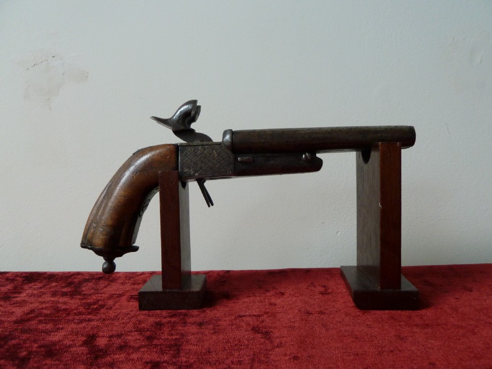 A nineteenth-century double-barrelled rimfire pistol with patinated steel barrels and a contoured wooden grip resting on display stands. View II