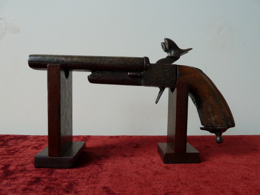 A nineteenth-century double-barrelled rimfire pistol with patinated steel barrels and a contoured wooden grip resting on display stands. View III