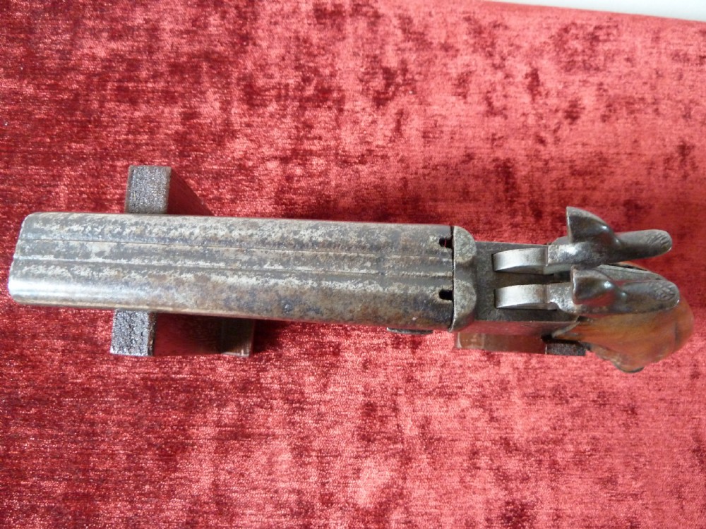 A nineteenth-century double-barrelled rimfire pistol with patinated steel barrels and a contoured wooden grip resting on display stands. View IV