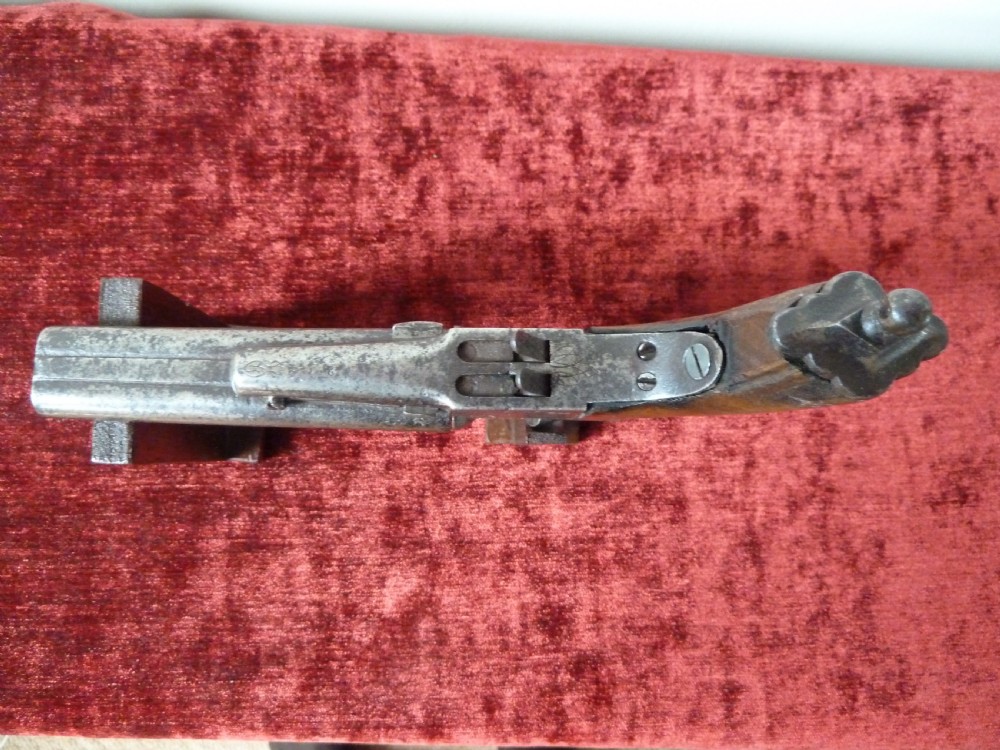 A nineteenth-century double-barrelled rimfire pistol with patinated steel barrels and a contoured wooden grip resting on display stands. View V