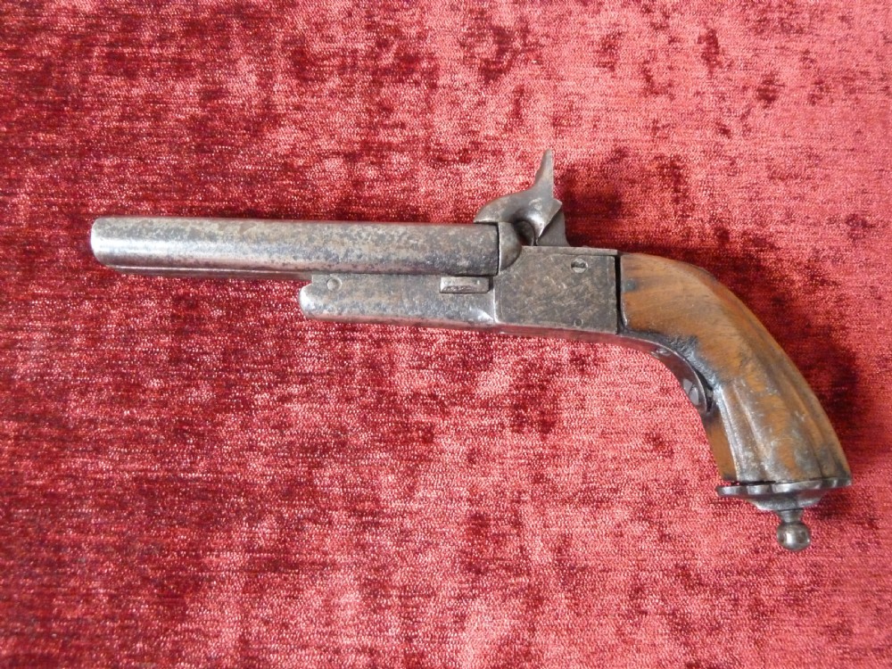 A nineteenth-century double-barrelled rimfire pistol with patinated steel barrels and a contoured wooden grip resting on display stands. View VI
