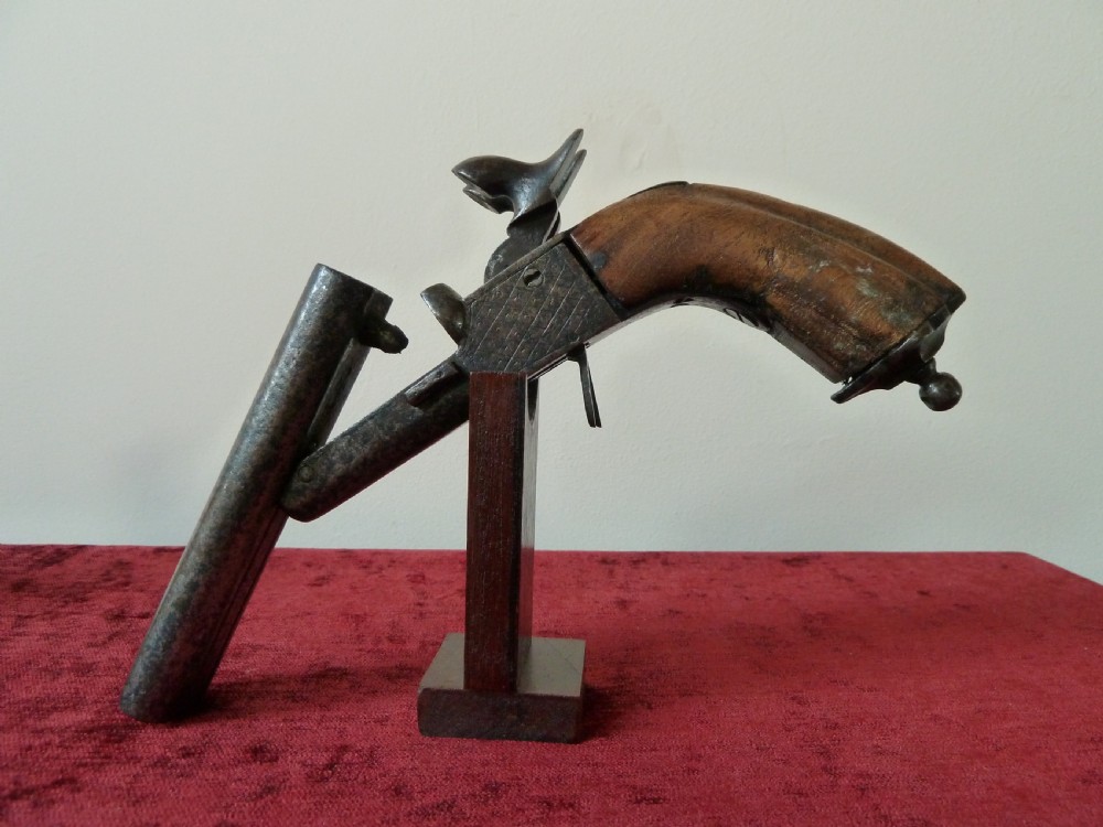 A nineteenth-century double-barrelled rimfire pistol with patinated steel barrels and a contoured wooden grip resting on display stands. View VIII