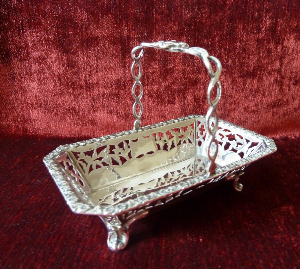An Edwardian rectangular sterling silver basket with pierced fretwork sides, a looped overhead handle, and four cast feet.